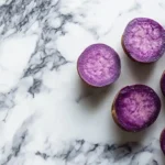 Vibrant purple sweet potatoes displayed on a marble background.